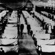 A historical photo of a flu hospital; rows of white-sheet partitions separate patients, and masked people stand in the corridors between them.