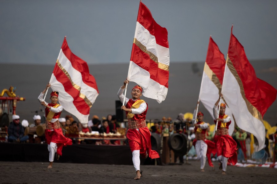 Four dancers perform with large flags in an open field.