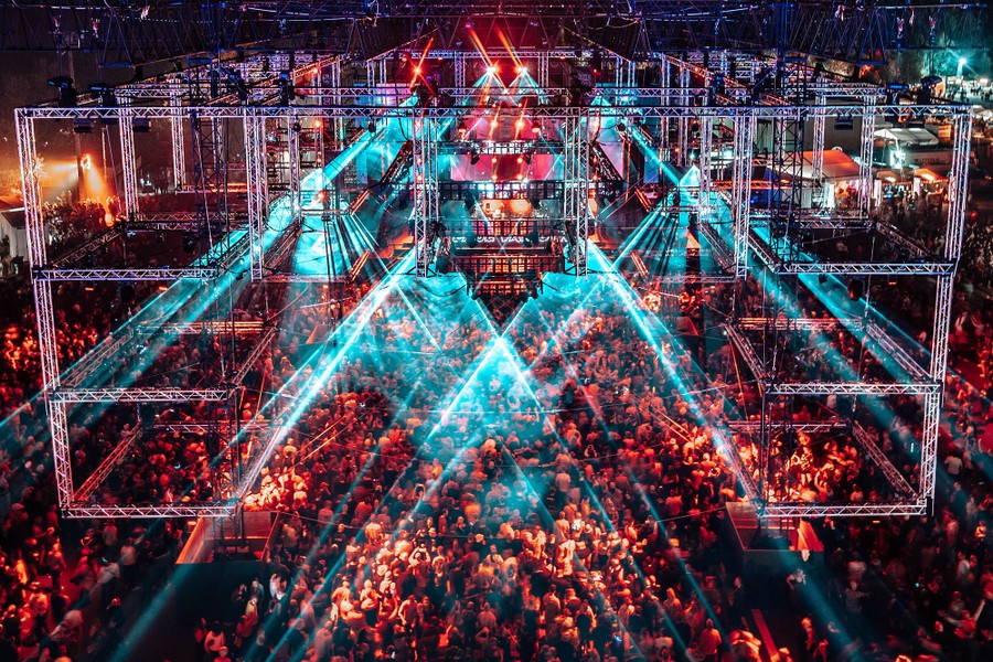 A wide view of a large crowd dancing beneath intricate stage lighting.