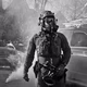 Black-and-white photo of a federal agent seen on a Minneapolis neighborhood street wearing a gas mask while tear gas goes off in the background.
