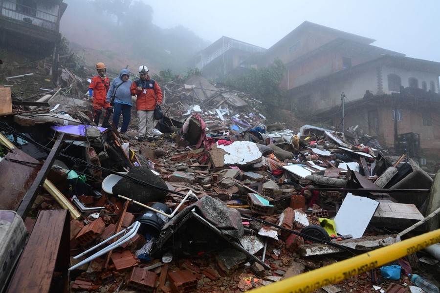 Rescue workers help a person walk through a debris-filled hillside following a landslide.