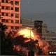 Photograph of flames bursting from an explosion on the side of a building at dusk