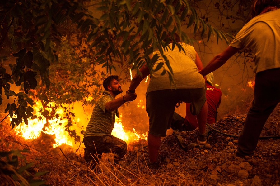 Several people help each other on a hillside as they battle burning foliage.