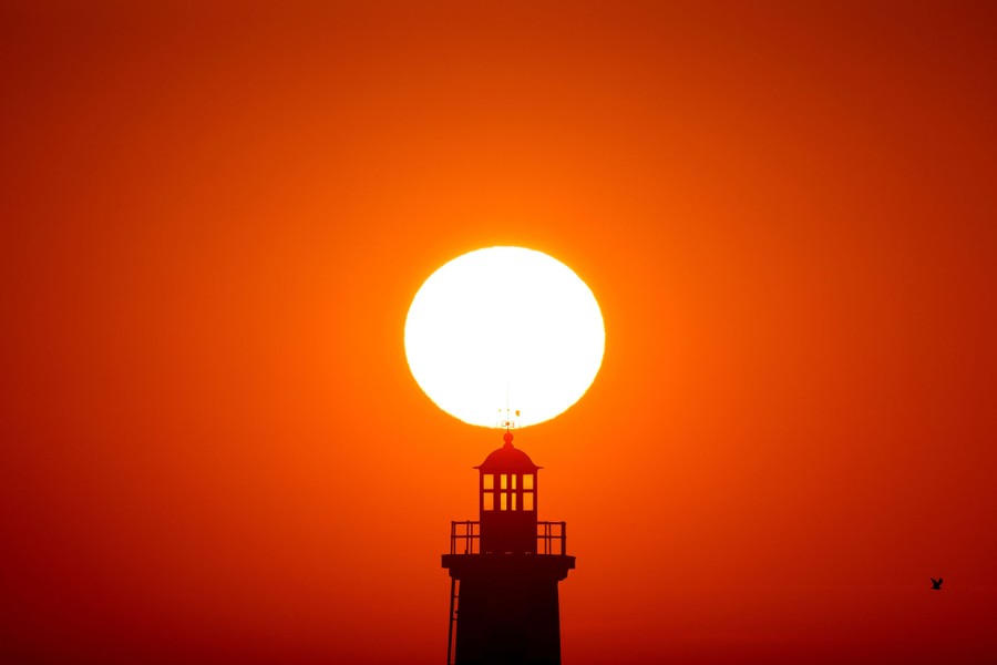 A low sun is seen above a lighthouse.