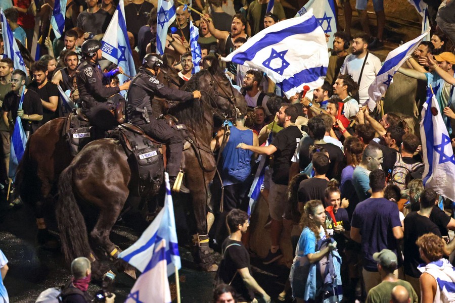 Two riot police officers sit on horseback among a group of protesters.