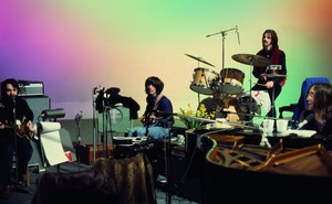 The Beatles sit at a variety of instruments, playing.