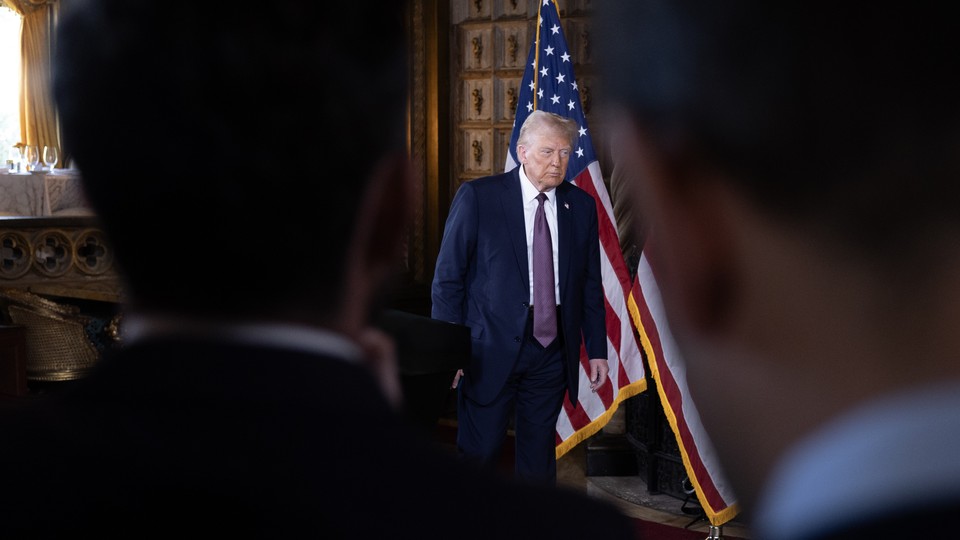 Donald Trump stands during his press conference between the silhouettes of two men in the crowd