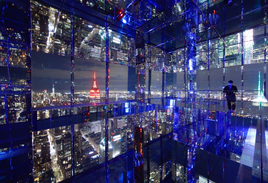 A person stands in a mirrored observation-deck room at night.