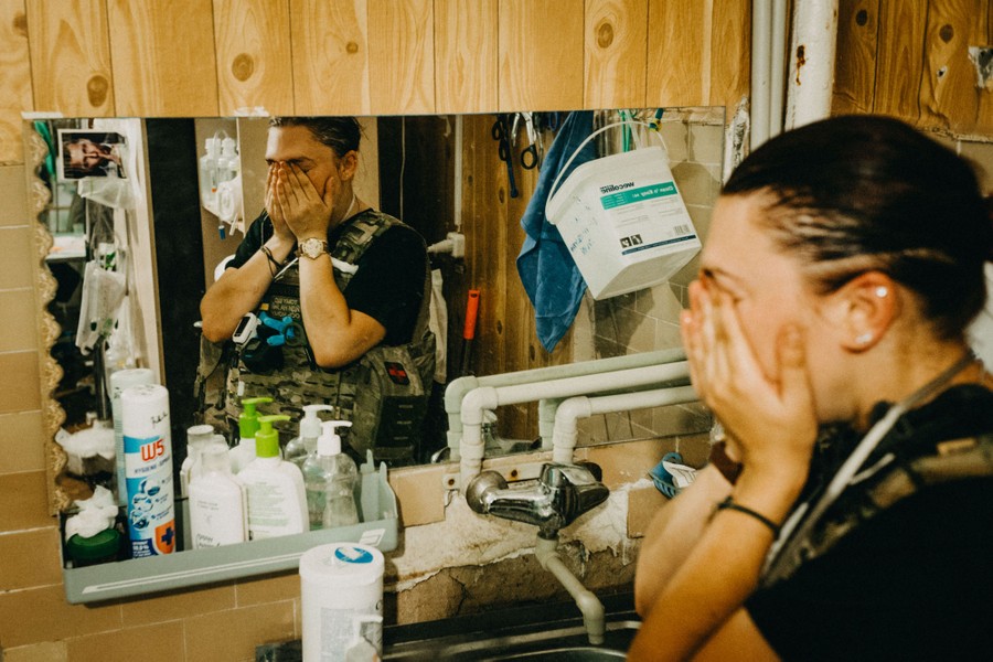 A military medical worker holds their hands to their face, seen reflected in a mirror.