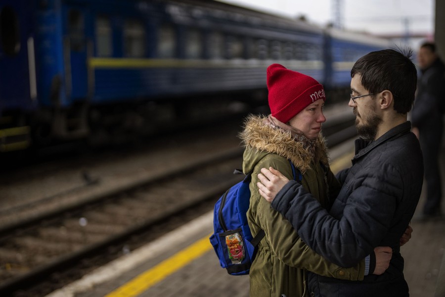 A man and a woman share an emotional embrace on a train-station platform.