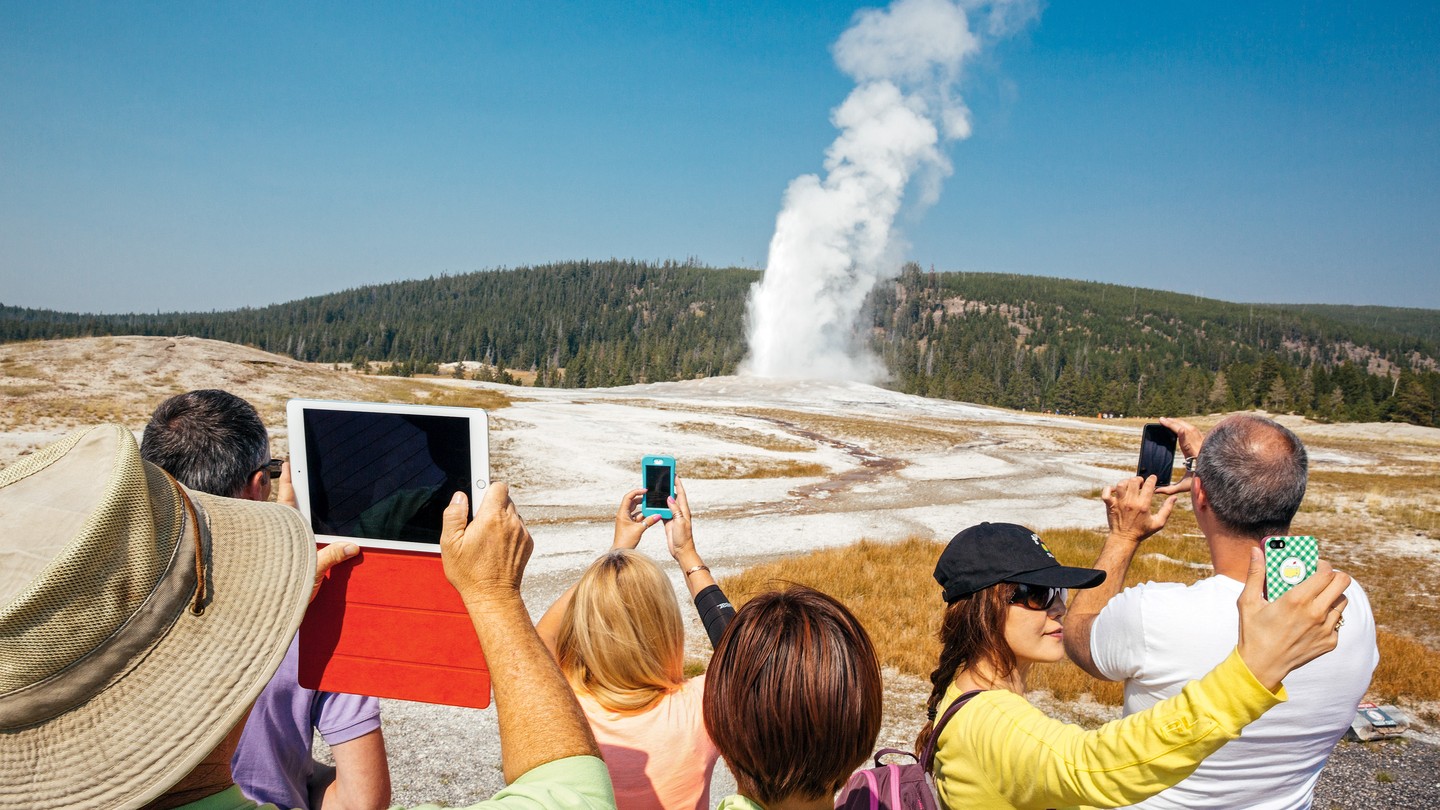 photo of crowd of people holding up phones and tablets to take pictures of geyser spout