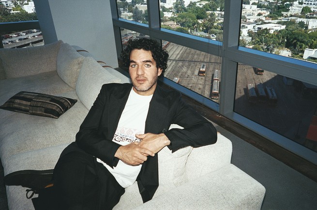 A color photograph of Benny Safdie on a white couch