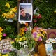 A memorial for a Colombian man killed in Maine during an ICE vehicle stop includes flowers, a photo of him, and cardboard signs including one that says, "Immigrants Make America Great!"