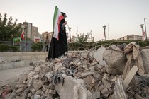 A veiled Iranian art student holds a country flag while standing on symbolic debris of a destroyed building as she performs in an anti-war conceptual play at a square in downtown Tehran, Iran