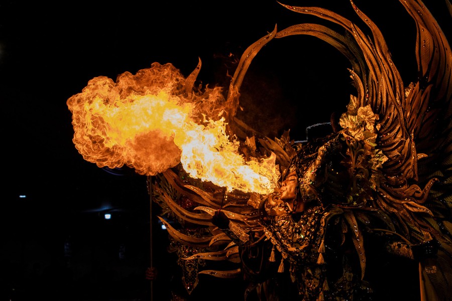 A performer in a large and elaborate costume spits out a fireball.