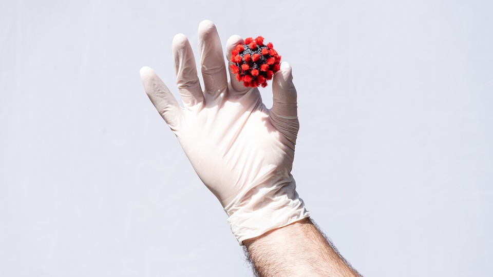 A white gloved hand holds a COVID-19 virus