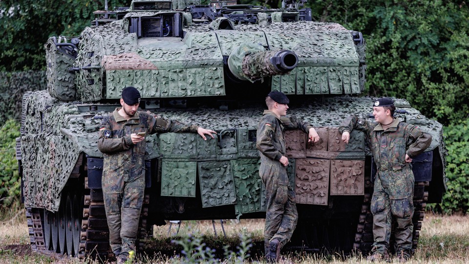 German armed forces stand at ease in front of a battle tank.