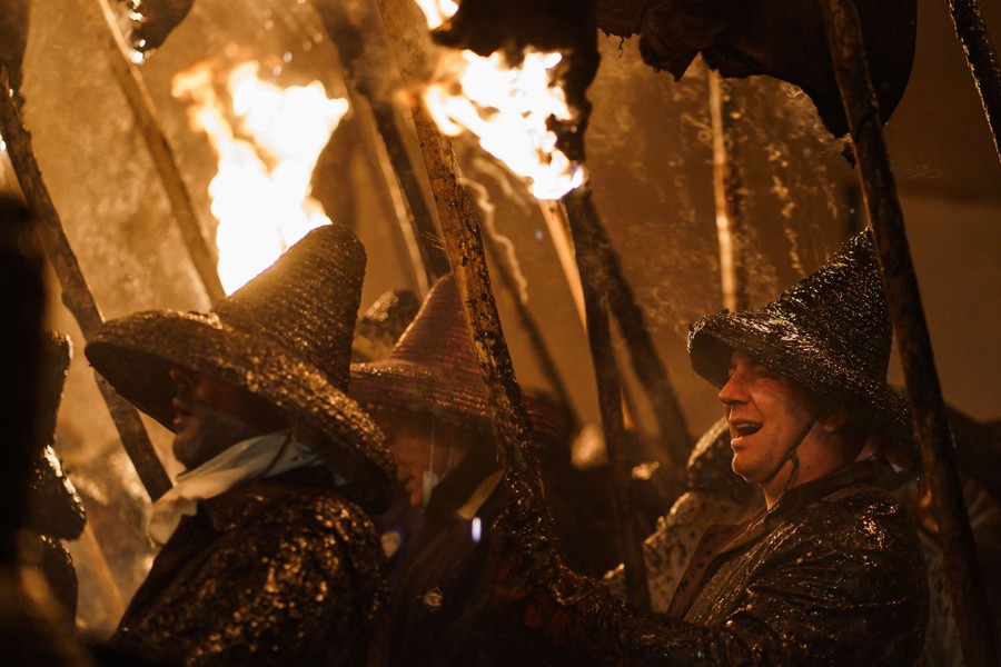 Several people wearing traditional protective clothing in a procession, carrying flaming torches