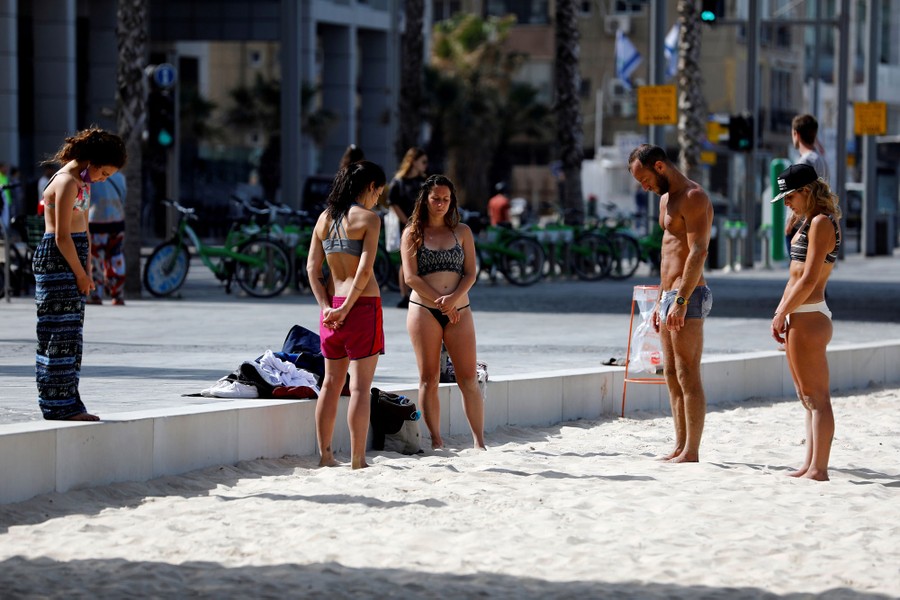 People stand still, heads bowed, along a beach.