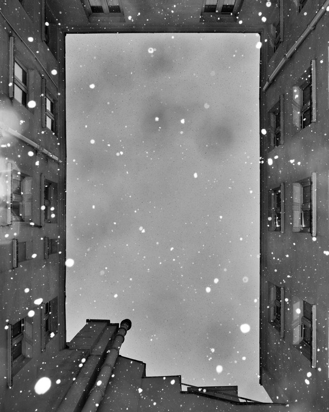 Black-and-white image of snow falling between buildings