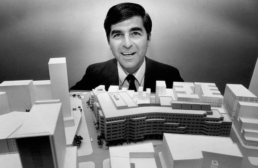 A man stands behind an architectural model of a large office building.
