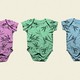 A row of baby onesies: one pink, one green, and one blue, each covered in a similar bamboo print.
