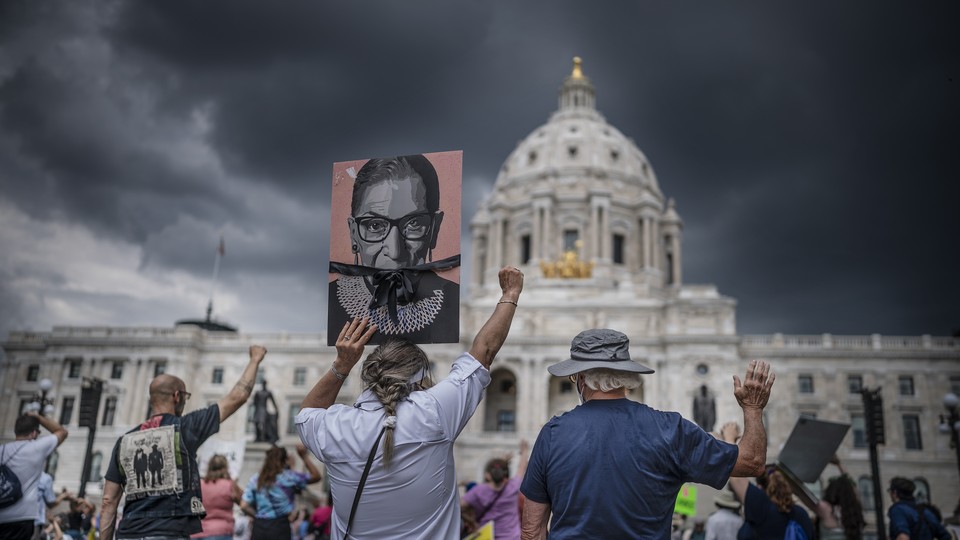 A group of protesters seen from behind raising signs and their fists, in front of the state capitol in St. Paul, Minnesota, in 2022