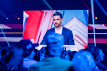 A giant television screen displays Ben Shapiro talking at a conservative conference, as viewers watch in the foreground.