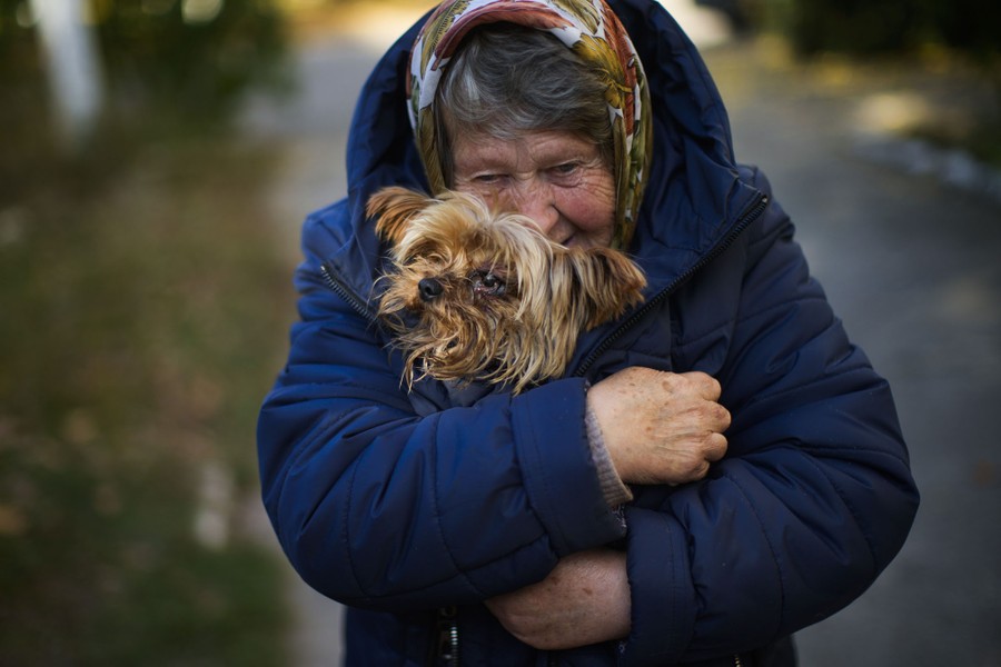 A woman holds a small dog close, wrapped in her coat.