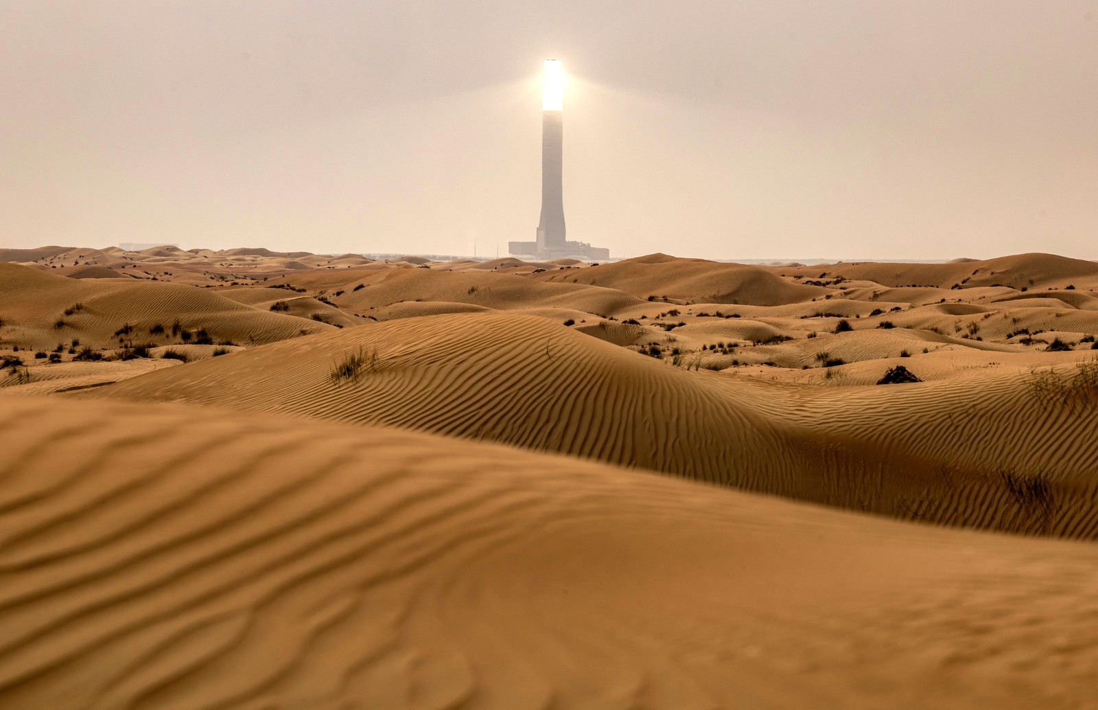 A distant view of a glowing solar tower, seen among many sand dunes.