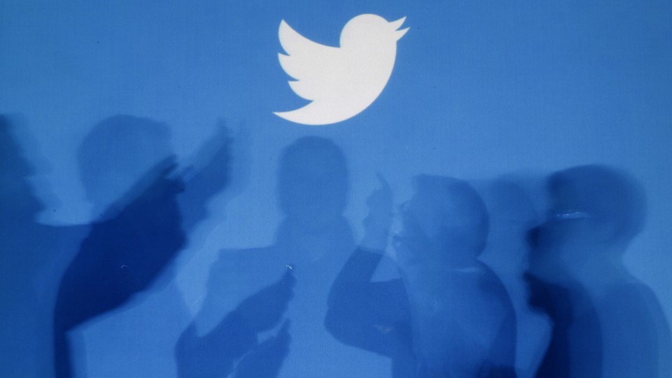 The shadows of people using smartphones against a blue backdrop with the Twitter logo