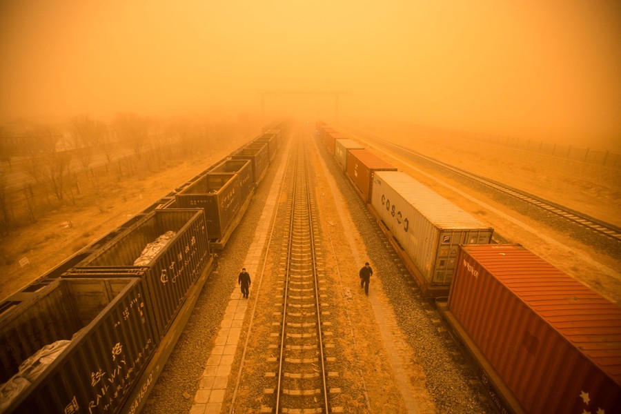 An elevated view of a rail yard beneath an orange sky, during a sandstorm