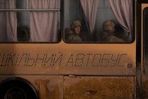 Two soldiers look out the window of a school bus.