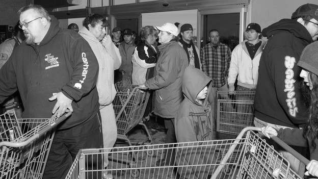 Customers push shopping carts while crowded in a small room.