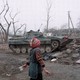 A women walks past a tank and ruins.