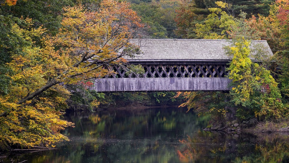 A covered bridge is flanked by autumn leaves beginning to change color along the Contoocook River in Henniker, New Hampshire, on October 6, 2023.
