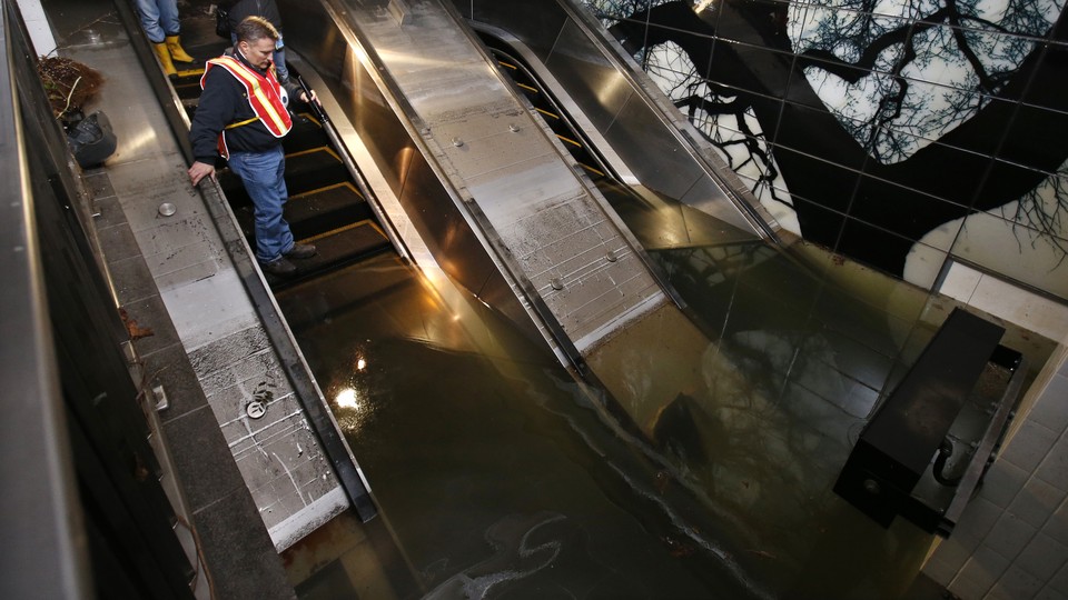 A man in a construction vest stands on a flooded escalator in a subway station.