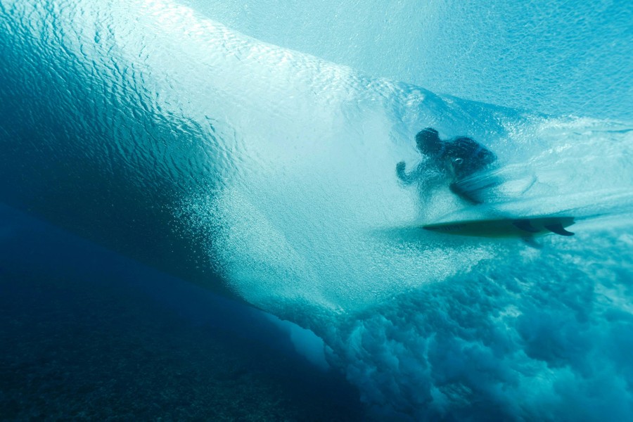An underwater view looking up toward a surfer riding a wave