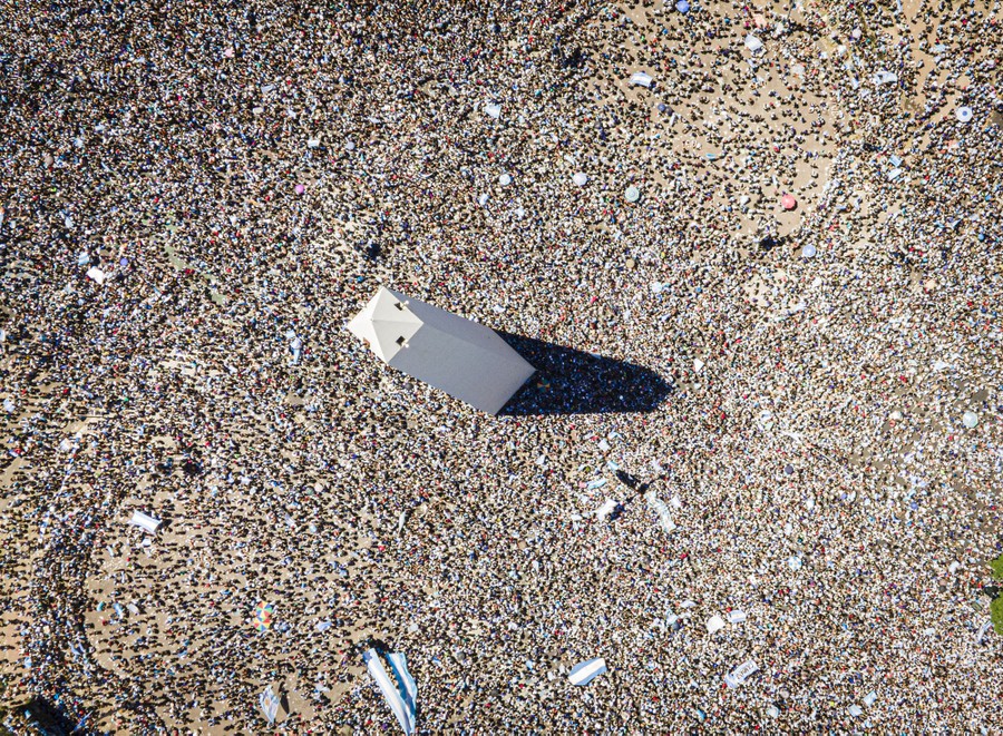 An aerial view of a tall monument, with thousands of people gathering below.