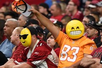 Fans wearing emoji masks wave from the stands at an NFL game.