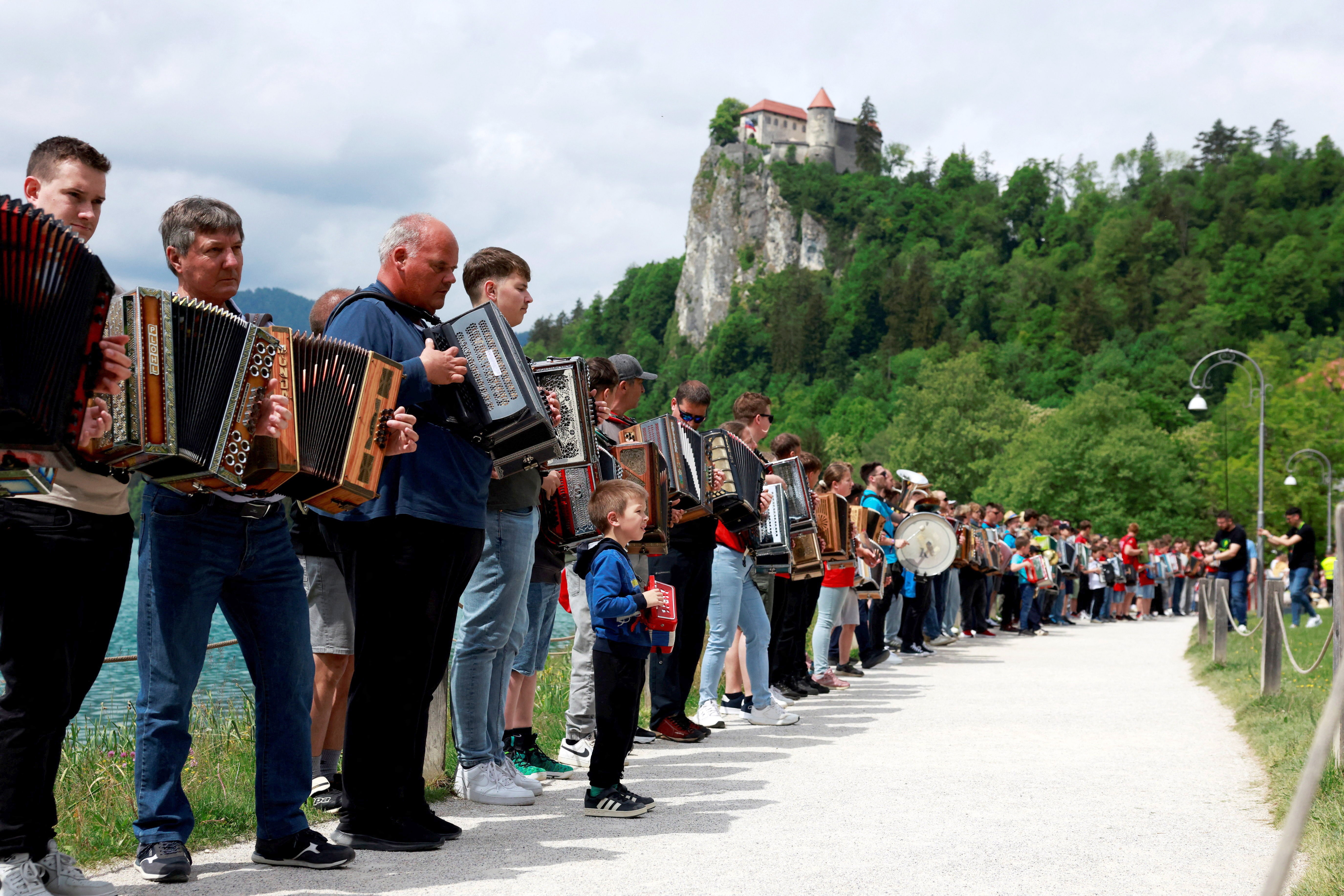 Dozens of accordionists stand side-by-side along a path during a mass performance.