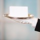 White gloved hand in black suit holds a blank notecard on a silver platter.