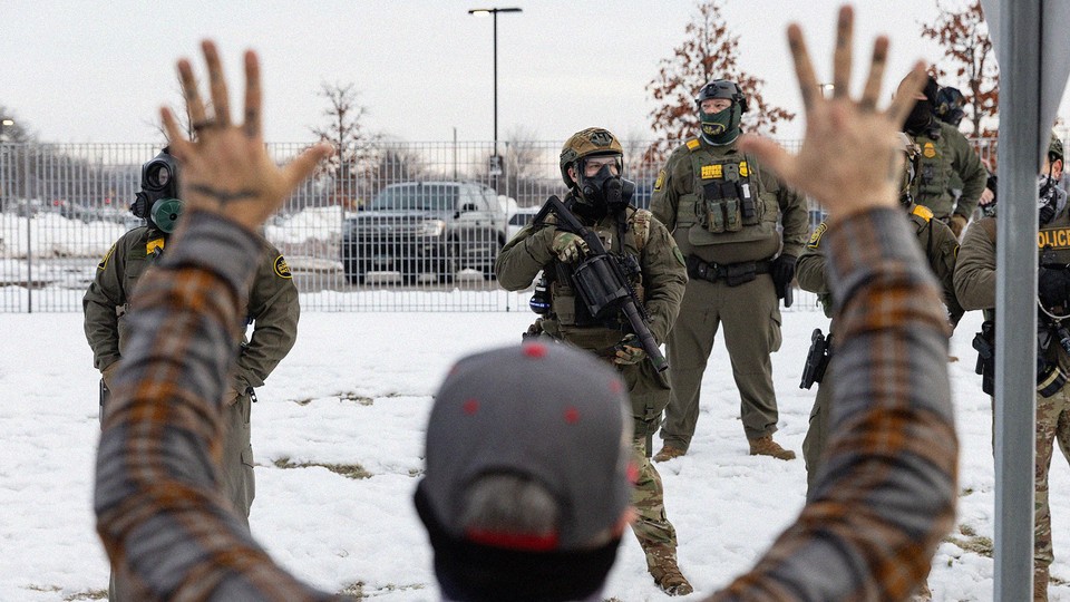 A man standing with his hands up opposite a group of heavily armed ICE agents