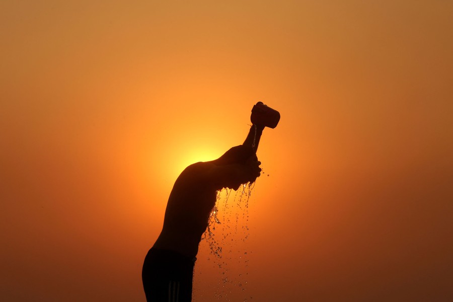A person is silhouetted against the setting sun as they cool off by dumping water on their head.