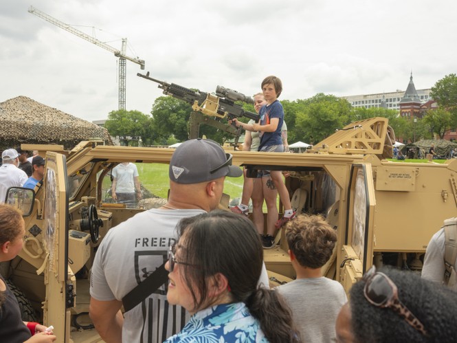 Picture of children climbing inside a tactical vehicle, part of a display of military equipment parked on the National Mall.