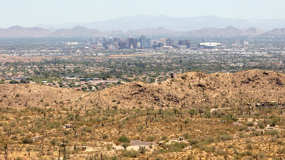 Phoenix, Arizona, from South Mountain Park on June 18, 2020. There are brown hills in the foreground, and the city's skyline in the background.