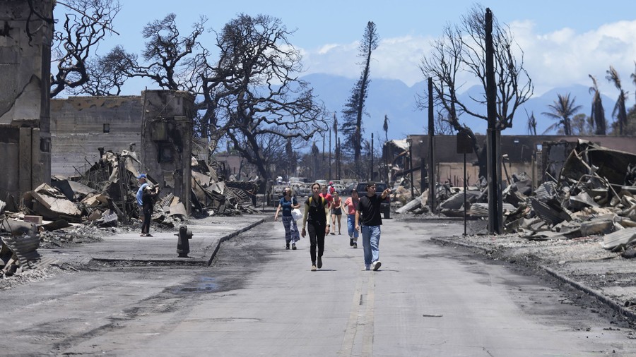 People walk along a street past wildfire damage.