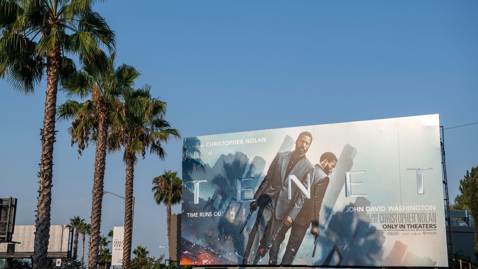 A billboard, showing the actor John David Washington, next to palm trees and against a blue sky
