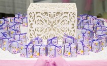 An ornate box sits on a table surrounded by small packages wrapped in floral paper and ribbon tied in a bow.