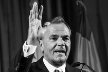 A black-and-white photograph of Rick Caruso at a podium